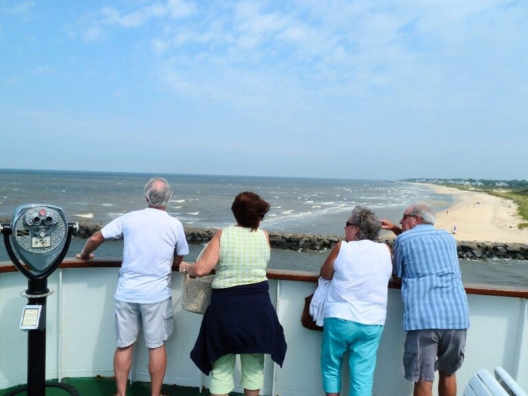 A group of people stand on the top deck of the Cape May - Lewes Ferry watching as the vessel sails out of Cape May