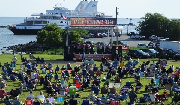 Concert-goers sit on their lawn chairs on the "green" next to the Cape May Ferry terminal in front of the stage, with the Ferry sailing in the background